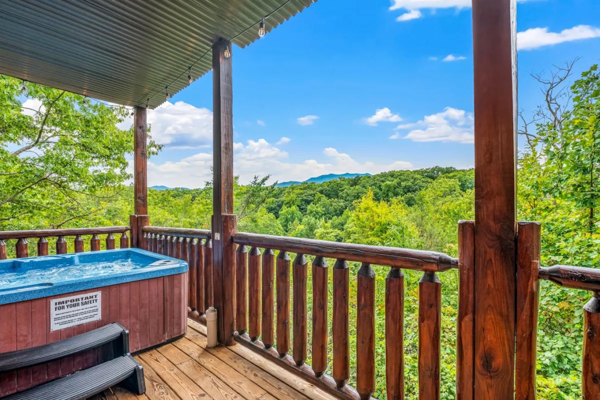 A tranquil outdoor hot tub sits on a wooden deck, framed by a sturdy railing and with uninterrupted views of the rolling Smoky Mountain ridges beyond. The setting invites guests to soak while immersed in natural beauty, with the sky above ideal for stargazing or relaxing after a day of hiking.