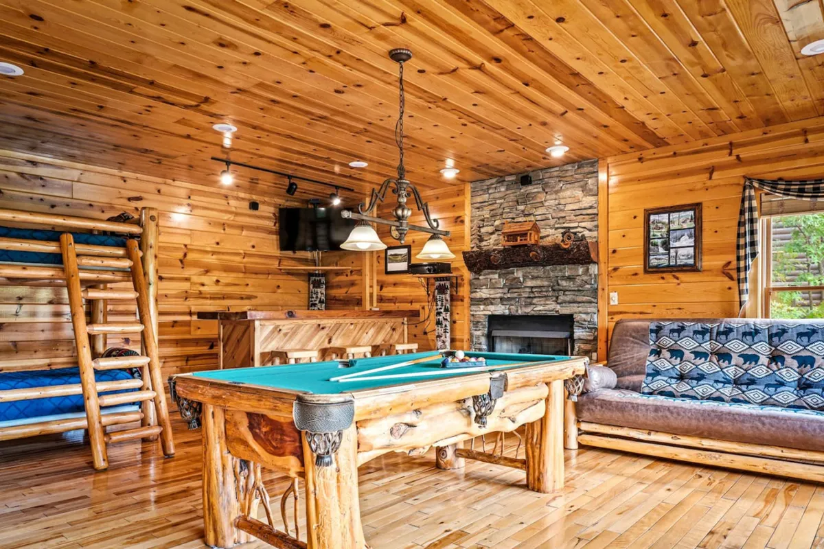 This image showcases a lively game room featuring a pool table, a wooden bunk bed, a stone fireplace, and a comfortable sofa. The space feels relaxed and playful, with plenty of room for both competitive games and cozy gatherings. The warm lighting and rustic finishes emphasize comfort and camaraderie.