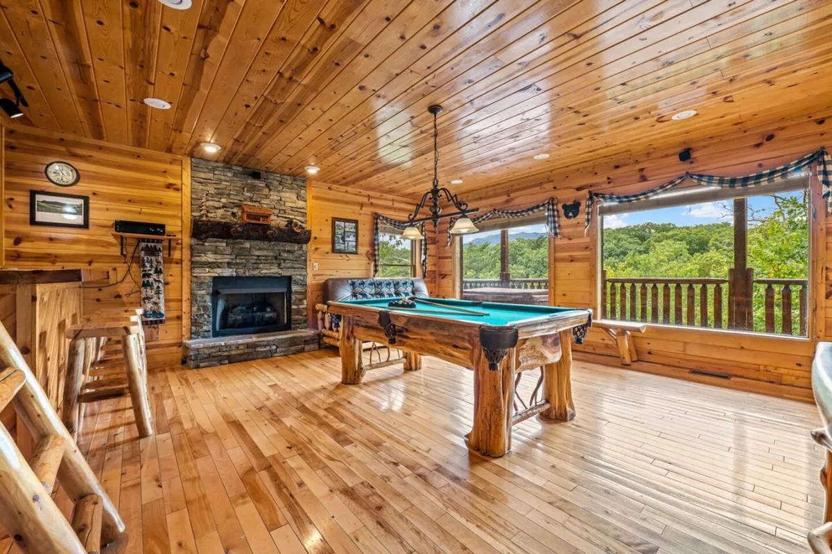 A vibrant game room featuring a pool table, cozy fireplace, and large windows with scenic views. The space is designed for family fun, with ample room for games, relaxation, and socializing after days of adventure.